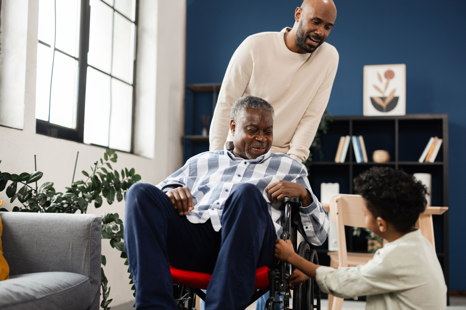 Senior man in a wheelchair is being supported by his son and grandson