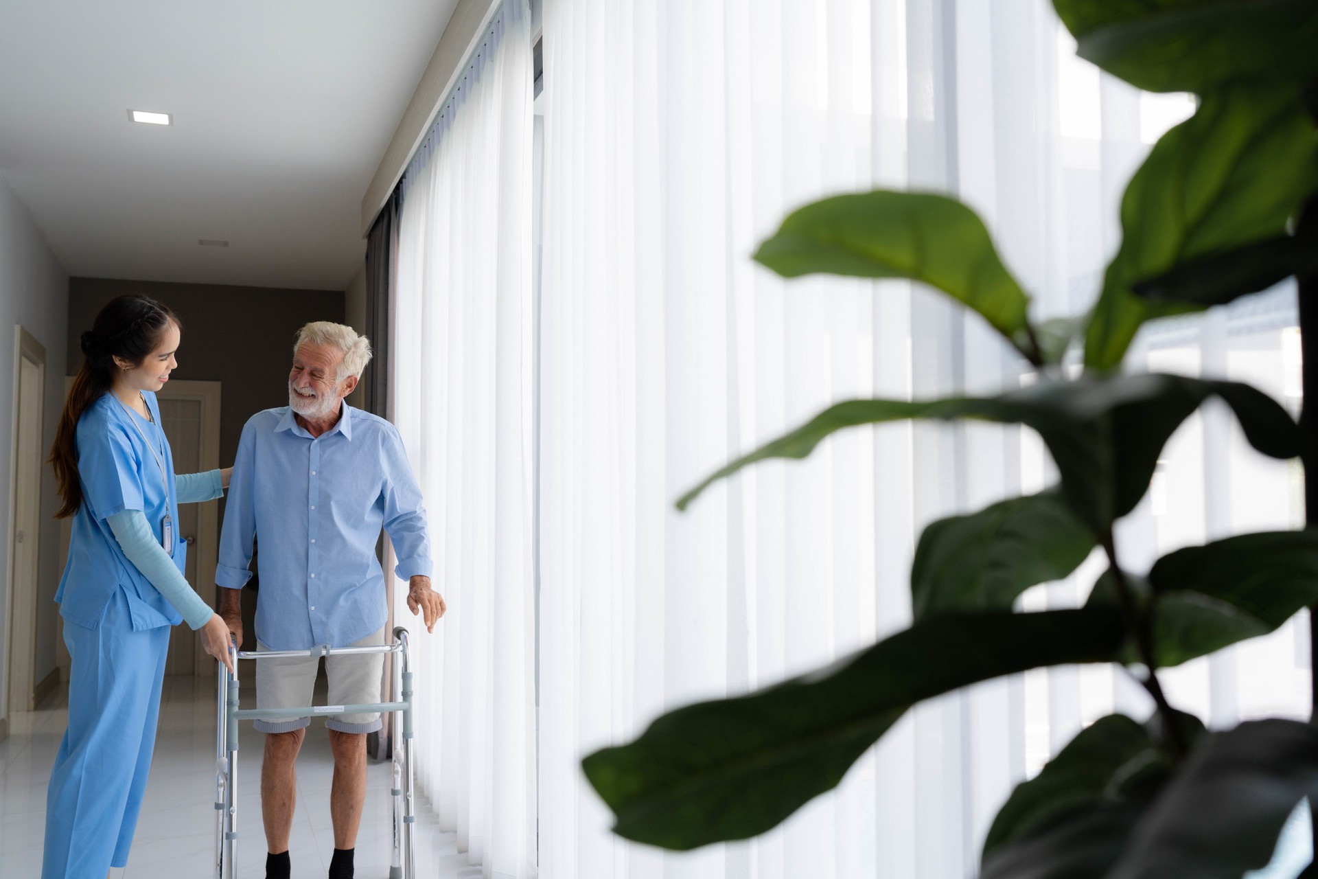 Home caregiver helping senior man walking at home.